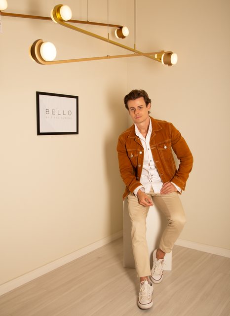 O pendente linear da Bello atravessando o canto do ambiente, com o designer ao fundo.