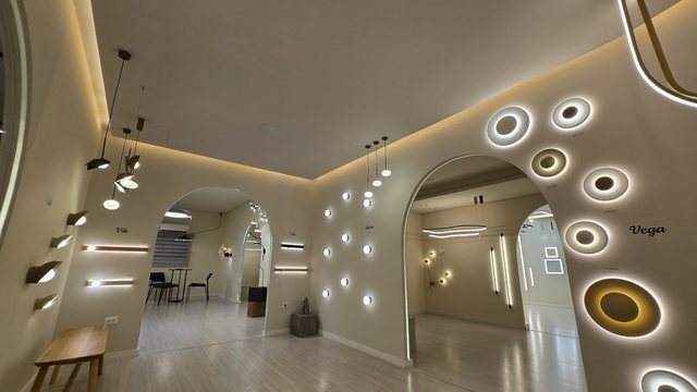 Corredor do showroom da Usina, com arandelas circulares acesas no arco