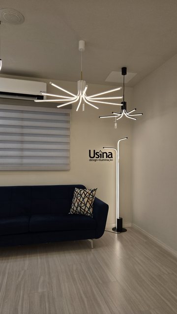 Estar do showroom da Usina, com sofá, luminária de piso e lustre aceso